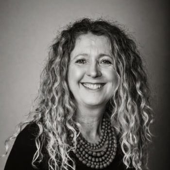 Black and white portrait of a smiling woman with curly hair wearing a beaded necklace.